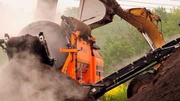 backhoe feeds compost into a shredder